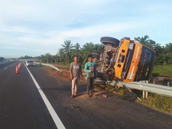 Sebuah dump truk tronton bermuatan batu split terbalik menerobos pagar pembatas jalan tol Pekanbaru-Dumai, Sabtu. 